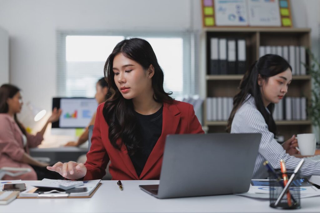 Lady wearing red coat working in front of her laptop — Business process outsourcing & offshore staffing | Sourcefit