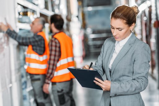 female inspector writing something while men working behind in storehouse — Business process outsourcing & offshore staffing | Sourcefit